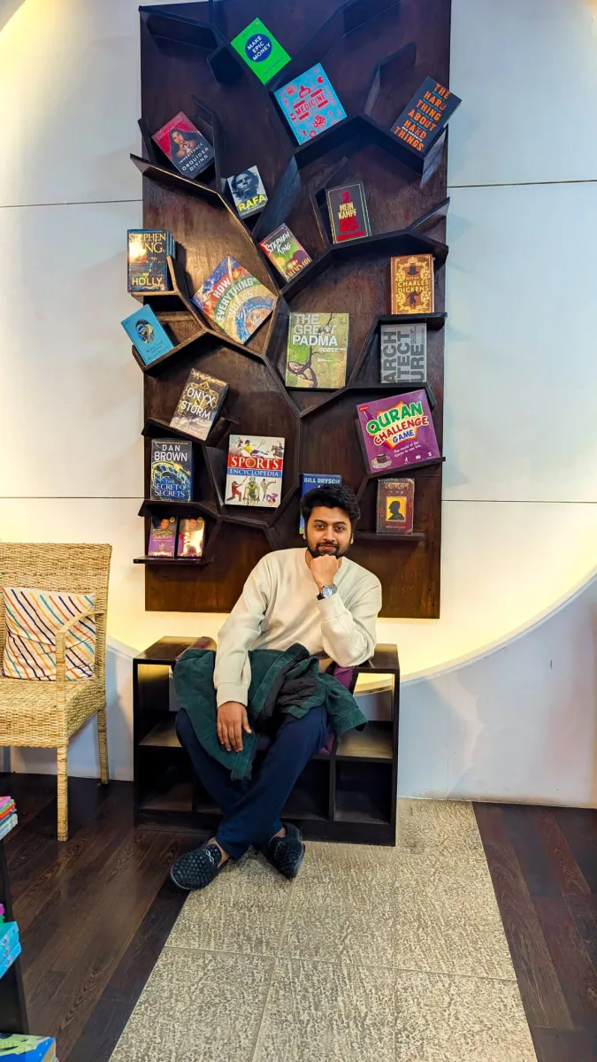 Mir Ahadul Islam sitting in front of a tree-shaped bookshelf filled with colourful books